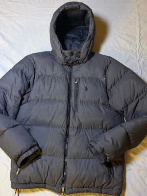 Ralph Lauren dunjacka mörkgrå – Strl M – Mycket bra skick (lagning + små hål) - Sjukt snygg och unik Ralph Lauren dunjacka i mörkgrå färg, storlek M, i mycket bra skick. Finns några små hål samt en lagning, vilket är medräknat i priset och påverkar inte funktionen.  Perfekt jacka för dig som vill ha en unik Ralph Lauren-jacka med karaktär.  Mått: Undersida: 47 cm Längd: 64 cm  • Märke: Ralph Lauren • Färg: Mörkgrå • Storlek: M • Skick: Mycket bra (se info ovan)  Ralph Lauren 3