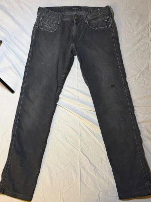 Replay Anbass jeans mörkgrå – Slim fit – 30/34 – Mycket bra skick (snygg slitning) - Säljer ett par Replay Anbass jeans i mörkgrå färg, slim fit, storlek 30/34, i mycket bra skick. Har en snygg slitning som ger en modern och stilren look.  Anbass är en av Replays mest uppskattade modeller med perfekt balans mellan komfort och passform.  Mått: Midja: 40 cm Längd: 96 cm  • Märke: Replay • Modell: Anbass • Passform: Slim  Replay 5