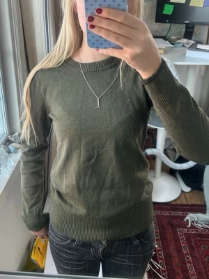 Grön stickad tröja  - En enkel och stilren olivgrön tunt stickad tröja med rund halsringning och ribbade muddar vid ärmslut och nederkant. Tröjan har lång ärm och en klassisk passform som funkar till det mesta. Perfekt för lager på lager under höst och vinter.