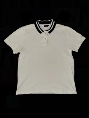 Vit piké från J.Lindeberg - Klassisk vit pikétröja från J.Lindeberg med marinblå detaljer på kragen och knappar framtill. Skön passform och stilren look som funkar till det mesta. Perfekt för dig som gillar enkel men snygg stil. Storlek L