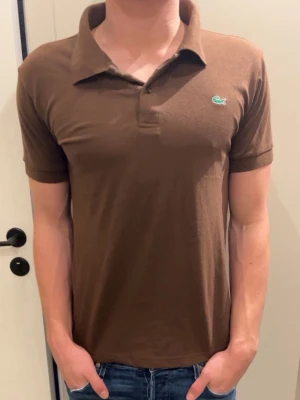 Brun pikétröja från Lacoste - Tja! Säjer nu denna feta lacoste piké lite schysstare såhär inför sommaren i storleken S!       Ny pris 1200kr modellen är 181cm och väger 70 kg