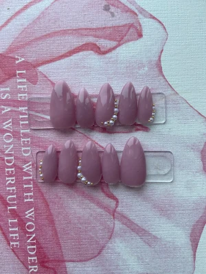 Rosa lösnaglar med pärldekor - Säljer ett set med snygga lösnaglar i en mjuk rosa nyans. Naglarna har en elegant mandelform och vissa är dekorerade med små vita pärlor och guldfärgade detaljer för extra lyxig känsla. Perfekt för dig som vill ha en chic och trendig look.