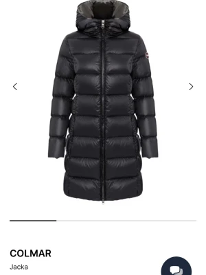 Svart lång pufferjacka från Colmar - Säljer en svart lång pufferjacka från Colmar med huva och dragkedja framtill. Jackan har en quiltad design och är perfekt för kalla dagar. Klassisk look med Colmar-logga på ärmen och en skön, vadderad känsla.