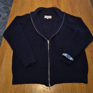 Mörkblå stickad kofta Maison Margiela - Tjena! Säljer en mörkblå ribbstickad kofta från Maison Margiela då den inte passar mig. Koftan är knappt använd endast ett fåtal ggr, den har hel dragkedja framtill, hög krage och långa ärmar. Klassisk och stilren design med diskreta vita sömmar i nacken. Perfekt för lager på lager under dessa och de kommande kyliga dagarna. Om du undrar något tveka inte med att höra av dig💫