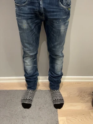 Replay Anbass blå jeans med färgstänk - Säljer ett par Replay Anbass jeans i blå tvätt med coola slitningar och färgstänk i gult och vitt. Jeansen har normal passform, klassisk femficksdesign och snygga kontrastsömmar. Materialet är jeans med stretch för extra komfort. Skriv om ni har frågor eller funderingar ‼️