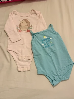 Blå body från Carter's 12m - Säljer en ljusblå ärmlös body från Carter's med trycket 'mommy & me by the sea' och små moln och fåglar framtill. Bodyn har smala axelband och knäppning i grenen. Perfekt för varma dagar.