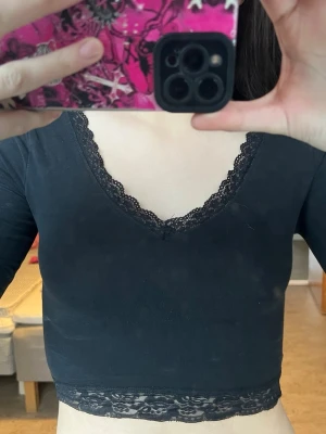 Svart långärmad topp med spets - Snygg svart långärmad topp från Even&Odd med v-ringning och fina spetsdetaljer vid halsringning och nederkant. Modellen är croppad och har en feminin look som passar perfekt till jeans eller kjol.