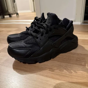  Nike Air  sneaker - Säljer ett par helsvarta Nike Air Huarache sneakers med chunky sula och klassisk logga på plösen. Skorna har en mix av skinn och syntetmaterial, snörning och en sportig vibe. Perfekta för dig som gillar streetstyle och vill ha något som sticker ut.