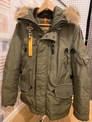 Grön Parajumpers parkas med päls - Säljer en grön Parajumpers parkas med pälsdetalj på huvan, flera fickor och snygga detaljer som gul rem och patch på ärmen. Jackan har dragkedja, knappar och är långärmad. Perfekt för kalla dagar och riktigt stilren look. KVITTO FINNS!!!