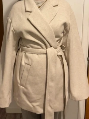 Beige Kappa lager157 - Snygg beige kappa från 157 i omlottmodell med bälte i midjan. Helt oanvänd. Passar folk som bär storlek S också