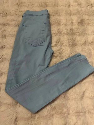 Ljusblå skinny jeans från Gina tricot - Säljer ett par ljusblå skinny jeans  i storlek 38. Byxorna har klassisk femficksdesign, bälteshällor och stängs med knapp och dragkedja. Materialet är mjukt och stretchigt 
