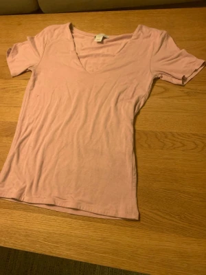 Ljusrosa v-ringad t-shirt - Enkel och mjuk ljusrosa t-shirt med v-ringning och korta ärmar. T-shirten har en slim passform och är tillverkad i bomull, perfekt för en avslappnad och stilren look.