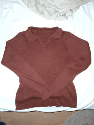 Brun långärmad pikétröja - Säljer en brun pikétröja med krage och v-ringad hals. Tröjan har lång ärm och är ribbstickad vilket ger en snygg struktur. Perfekt för dig som gillar en enkel men stilren look.
