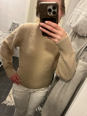 Beige stickad tröja med rund hals - Säljer en enkel och stilren beige stickad tröja med rund halsringning och långa ärmar. Tröjan har ribbade muddar vid ärmslut och nederkant, perfekt för lager-på-lager under kyliga dagar.