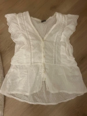 Vit blus  - En vit blus med volanger. Den är i storlek L vilket för mig känns lite konstigt då den sitter perfekt på mig som vanligtvis har S. Skriv om ni vill ha bild hur den sitter på så fixar jag. Den är använd nån enstaka gång men ser helt ny ut. 