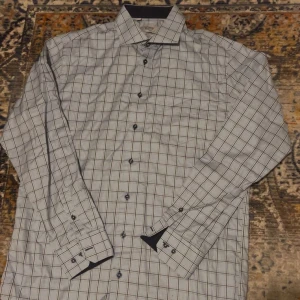 Rutig skjorta Oscar of Sweden  - Snygg rutig skjorta från Oscar of Sweden i storlek L. Skjortan är ljusblå med mörkblå och vita rutor, har långa ärmar och klassisk krage. Tillverkad i bomull och har knappar framtill. Perfekt för dig som gillar stilrena mönster. Väldigt fint skick 