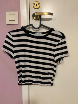 Randig croppad topp från Zara - Säljer en svartvit randig croppad topp från Zara. T-shirten har korta ärmar och rund halsringning. Materialet är mjukt och stretchigt, perfekt till jeans eller kjol. Klassisk och enkel design som alltid funkar.