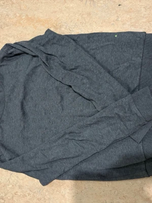 Grå långärmad tröja från BOSS - Säljer en stilren grå långärmad tröja från BOSS med slim fit passform. Tröjan har en rund halsringning med en snygg röd detalj på insidan av kragen. Perfekt för dig som gillar enkel och clean stil.