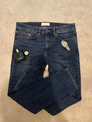 Mörkblå jeans från Pier One - Säljer ett par klassiska mörkblå jeans från Pier One. Jeansen har fem fickor, kontrastsömmar och en snygg läderpatch bak i midjan. Materialet är slitstarkt jeans och passformen är rak med normal midja. Perfekta till sneakers eller boots. W30 L30