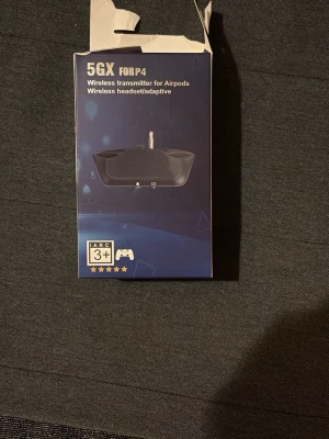 5GX Wireless Transmitter for PS4 - Trådlös sändare för PS4-kontroller, kompatibel med AirPods och andra trådlösa hörlurar. Möjliggör trådlös ljudöverföring från PS4 till hörlurar. Inbyggt batteri med upp till 8 timmars användning, laddas via USB. Kartongen är öppnad men produkten ser ut att vara i gott skick.