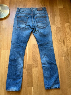 Nudie Jeans Thin Finn blå jeans - Säljer ett par Nudie Jeans Thin Finn i klassisk blå tvätt med snygga slitningar och kontrastsömmar. Modellen har normal passform, raka ben och ikonisk broderad bakficka. Tillverkade i 100% bomull för en skön känsla och tidlös look. Thinn Finn, Used broken. Storlek 31/32