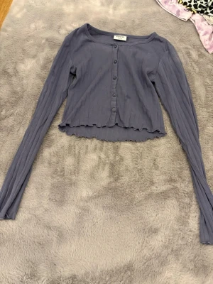 Ljuslila ribbad kofta från Kappahl - Säljer en ljuslila ribbad kofta från Kappahl i storlek 146/152. Koftan har långa ärmar, knappar framtill och en croppad passform med vågig kant nertill. Perfekt att slänga över ett linne eller t-shirt för en chill look.