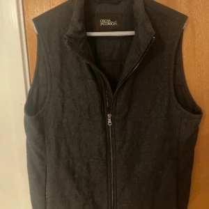 Väst från Oscar Jacobson - Snygg mörkgrå dunväst från Oscar Jacobson med quiltad design och hög krage. Använd väldigt lite. Absolut toppskick. Nypris 2900.