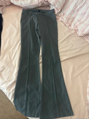 Gråa bootcut kostymbyxor - Snygga gråa kostymbyxor med bootcut passform och pressveck längs benen. Byxorna har hög midja och är gjorda i ett mjukt material som känns bekvämt hela dagen. Perfekta till en stilren look och passar till både sneakers och boots.