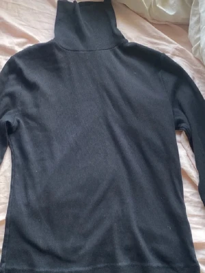 Svart polotröja från BikBok - Svart polotröja från BikBok i storlek L. Tröjan är ribbstickad med lång ärm och hög polokrage, perfekt för lager-på-lager under kyliga dagar. Enkel och stilren design som funkar till allt.