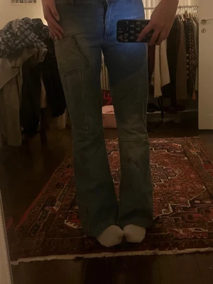 Blå bootcut jeans med detaljer - Säljer ett par ljusblå bootcut jeans med coola sömdetaljer.. Jeansen har flera dekorativa sömmar och fickor. Slitna nedtill (se sista bilden)