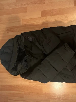 Svart pufferjacka från Canada Goose - Säljer en svart pufferjacka från Canada Goose i storlek M. Jackan har huva, dragkedja och två sidofickor sop gör den riktigt praktisk. Perfekt för kalla dagar när du vill hålla dig varm och ändå se stilren ut.