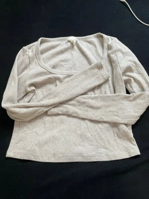 Beige ribbad långärmad topp - Säljer en beige ribbad topp med lång ärm och rundad urringning. Toppen är croppad och har en mjuk, stretchig känsla som gör den skön att bära. Perfekt att matcha med jeans eller kjol för en enkel och clean look.