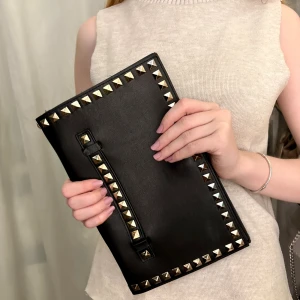 Svart kuvertväska med nitar - Säljer en svart kuvertväska i skinn med coola guldfärgade nitar runt kanterna och på handtaget. Väskan har en stilren och edgy look, perfekt för att lyfta vilken outfit som helst. Enkel att bära i handen. Inte zara, vet nt märke, köpt second hand