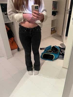 Svarta bootcut jeans - Säljer ett par svarta bootcut jeans med låg midja. Jeansen har klassisk femficksdesign, bälteshällor och är tillverkade i ett mjukt jeansmaterial. Passformen är slim upptill och lätt utsvängda nedtill för en snygg siluett.