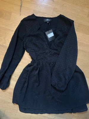 Svart prickig kortklänning Studio 21 - Supersnygg svart kortklänning från Studio 21 med diskret prickigt mönster, v-ringning och knappar framtill. Klänningen har lång ärm och resår i ryggen. Perfekt till fest eller vardags. Aldrig använd. Nypris 599kr. Storlek S/M 