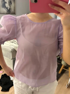 Lila Topp  - Genomskinlig lila topp från H&M med puffärmar. Jättebra skick och supercool till fest eller middag. Man kan nog säkert ha ett linne under om man är för obekväm.
