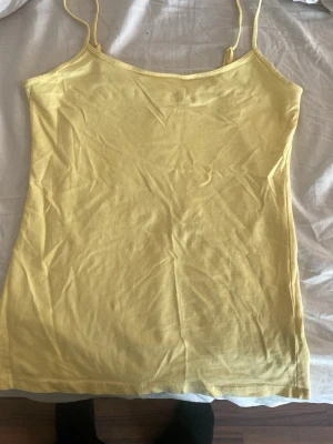 Gul linnetopp från Primark - Säljer en enkel och stretchig gul linnetopp från Primark med tunna axelband. Toppen är rak i modellen och gjord i mjuk bomullsblandning, perfekt för varma dagar eller som layering-piece.