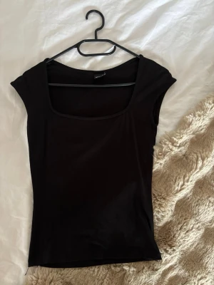 Svart topp med u-ringning Gina Tricot - En enkel och stilren svart topp från Gina Tricot i storlek XS. Toppen har en u-ringning och är ärmlös, vilket ger en clean och modern look. Tillverkad i mjukt bomullsmaterial som känns skönt mot huden. Perfekt att matcha med jeans eller kjol. Soft kollektionen.