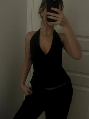 Svart omlott halterneck topp Nelly XS - Säljer en svart omlott halterneck topp från Nelly i modellen 'Amaze Me Wrap Top'. Toppen har djup v-ringning och knyt i nacken, vilket ger en snygg och smickrande passform. 