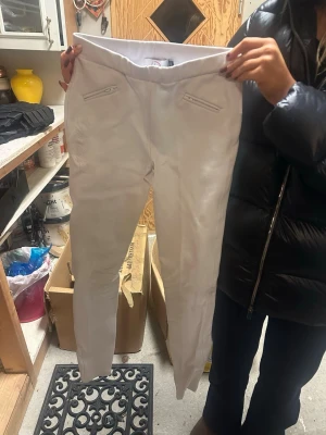 Vita ridbyxor från HKM, 158/164 - Säljer ett par vita ridbyxor från HKM i storlek 158/164. Byxorna har hög midja, dragkedjefickor framtill och förstärkning på insidan av benen för extra grepp. Stretchigt material som ger skön passform och rörelsefrihet.