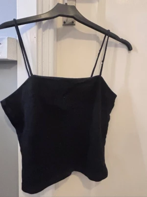 Svart ribbad linnetopp med smala band - En enkel svart linnetopp med smala axelband och rak skärning. Toppen är ribbad och har en croppad passform som passar perfekt till höga jeans eller kjol. Materialet känns mjukt och stretchigt, vilket gör den bekväm att bära under varma dagar.