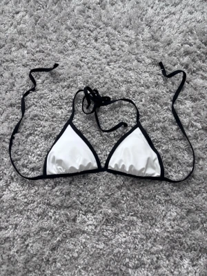 Vit bikiniöverdel  - Säljer en stilren trekantsbikini från 157 i storlek XS. Överdelen är vit med svarta kanter och tunna knytband i nacken och ryggen. 