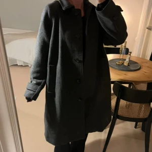 Mörkgrå kappa från H&M - Stilren mörkgrå kappa från H&M. Har knappt använt den! Storlek S