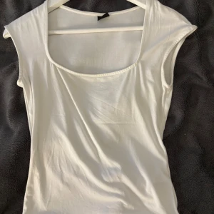 Vit ärmlös linnetopp - Säljer en stilren vit linnetopp med breda axelband och rundad urringning. Toppen är enkel och passar perfekt till jeans eller kjol. Tillverkad i mjukt bomullsmaterial för en skön känsla.