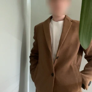 Brun kappa från New Look - Snygg brun kappa med rak passform och klassisk krage. Jackan har två knappar framtill och diskreta fickor på sidorna. Perfekt för dig som gillar stilrena och tidlösa plagg. Materialet känns mjukt och värmande, perfekt för kyligare dagar.