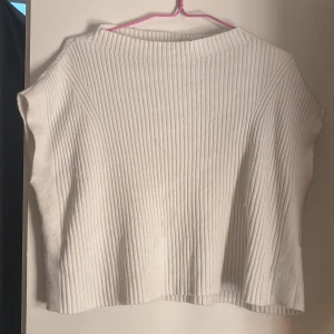 Vit ribbad topp från NA-KD - Säljer en vit ribbad topp från NA-KD med boxig passform och ärmlös design. Toppen har en högre rund halsringning och är tillverkad i ett mjukt, stickat material som känns skönt mot huden. Säljer då den inte kommer till användning 