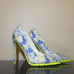 Färgglada pumps med mönster och hög klack - Unika pumps med höga klackar och spetsig tå. Skorna har ett färgstarkt mönster i blått, gult och vitt, samt en neongul sula med grovt mönster undertill. Perfekta för dig som vill sticka ut med din stil.