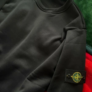 Svart sweatshirt från Stone Island - Svart sweatshirt från Stone Island med klassisk rund hals och ikonisk patch på ärmen. Tröjan har en clean look och är tillverkad i mjuk bomull. Perfekt för dig som gillar streetwear och vill ha något stilrent med tydlig logga. Priset kan även sänkas vid snabba affär