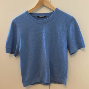 Blå stickad topp från Gina Tricot - Snygg ljusblå stickad topp från Gina Tricot med rund hals och korta ärmar. Enkel och stilren design som är perfekt för vår och sommar. Mjuk och skön kvalitet med ribbad kant vid hals och ärmslut. Passar dig som gillar klassiska och fräscha färger. Den har en liten fläck på en armen men man ser inte den framifrån 