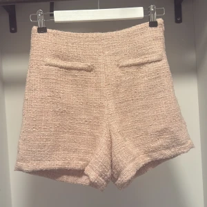 Rosa  tweed shorts med fickdetaljer - Snygga rosa shorts i tweed med hög midja och raka ben från Guess. De har två dekorativa fickor framtill och en mjuk, strukturerad yta som ger en exklusiv känsla. Perfekta för dig som gillar en chic och trendig look med lite Paris-vibe.